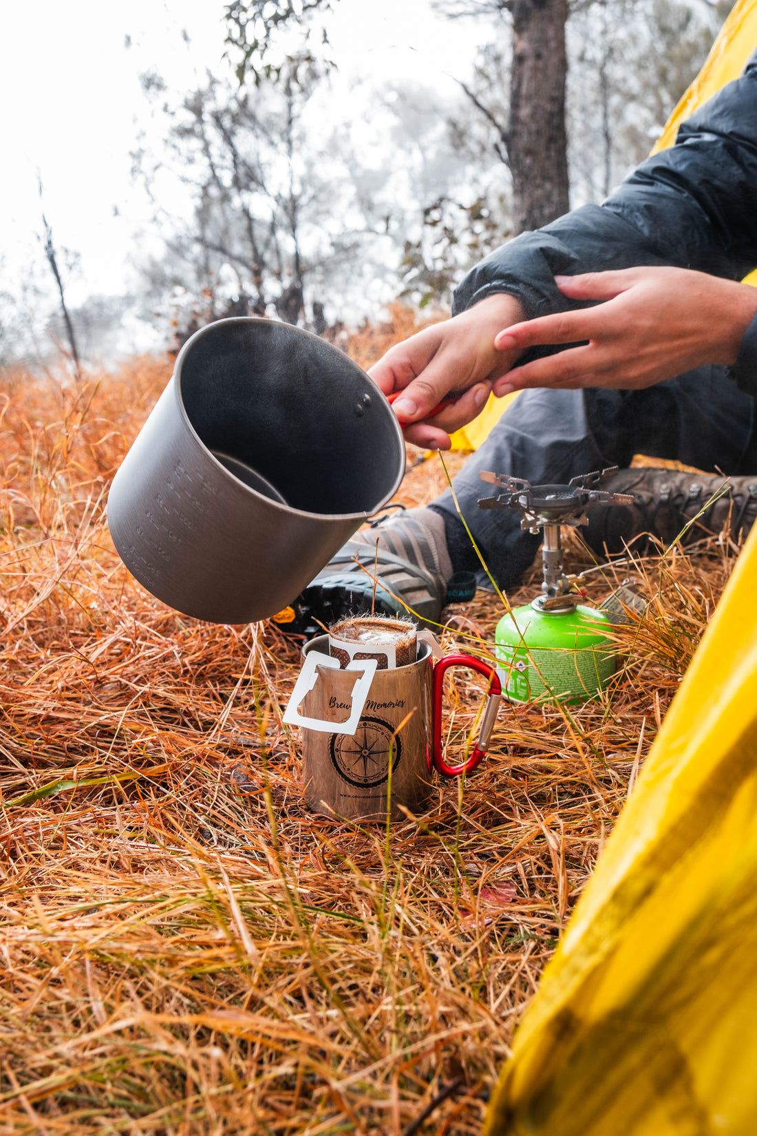 Pouring hot water from a camp pot into a Grounded Drops drip coffee bag on an enamel mug