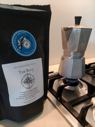 Moka pot on a gas stove next to a Grounded Drops Bunji coffee pouch
