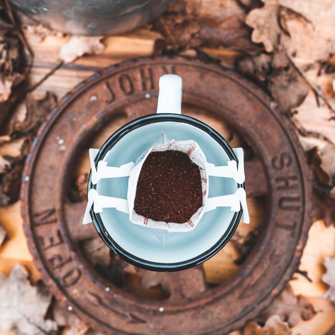 Open drip coffee bag hanging on an enamel mug among dry leaves