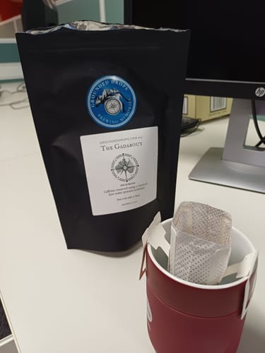 Grounded Drops Gadabout pouch and a drip coffee bag in a mug on an office desk