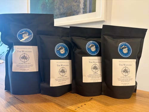 Sealed Grounded Drops coffee pouches lined up on a timber bench